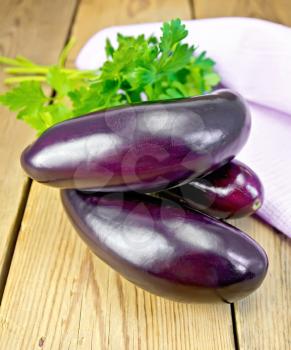 Ripe purple eggplants with parsley and a napkin on a wooden boards background