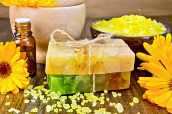 Two bars of homemade soap, yellow bath salt, oil in a bottle and marigold flowers on a background of wooden planks