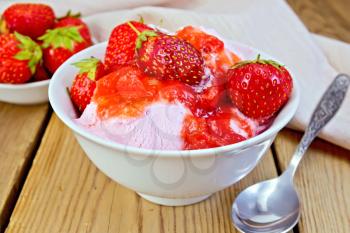 Strawberry ice cream in a white bowl with strawberries, a spoon, a napkin on a wooden boards background