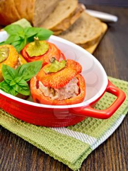 Three sweet peppers stuffed with meat and rice with basil leaves in red brazier on the green napkin, bread on a wooden boards background