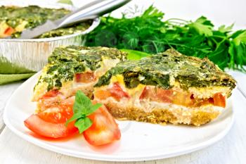 Two pieces of cake Celtic with spinach, tomatoes, oatmeal and eggs in a white plate in a baking dish from a foil on the background light wooden boards