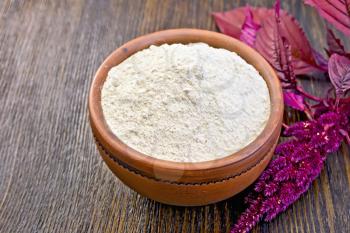 Amaranth flour in a clay bowl, purple amaranth flower on the background of wooden boards