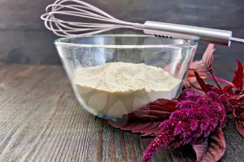 Amaranth flour in a glass bowl, blender, purple amaranth flower on the background of wooden boards