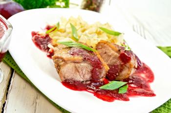 Roasted duck breast with stewed cabbage, green onions and plum sauce in a white plate on a towel, plum and parsley on a wooden boards background