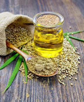Flour hemp in a wooden spoon, hemp seed in a bag and table, hemp oil in a glass jar, green leaves of hemp on a background of wooden planks