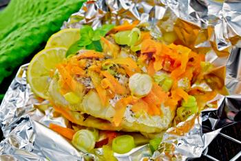 Pike with carrots, leek, basil and lemon slices in a foil on a metal grid, green towel on the background of wooden boards