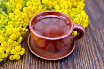 Herbal tea in a clay cup of fresh tansy flowers on the background of wooden boards
