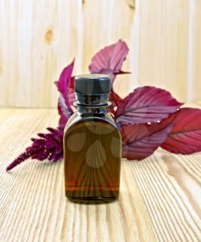 One vial of oil with a branch of burgundy amaranth on a background light wooden board