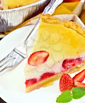A piece of strawberry pie with cream sauce, fork, strawberry, mint in white plate on a wooden boards background
