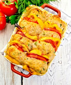 Cutlets of turkey meat baked with tomatoes and yellow pepper in a ceramic roasting pan on a towel, parsley on the background light wooden boards on top
