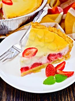 A piece of strawberry pie with cream sauce, fork, strawberry, mint in white plate on a dark wooden board