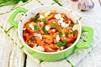 Shrimp and tomatoes baked with feta cheese in a green towel on a roasting pan, parsley and garlic on a wooden boards background