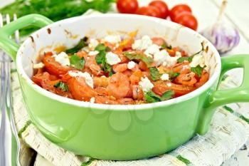 Shrimp and tomatoes baked with feta cheese in a roasting pan on a kitchen towel, parsley and garlic on a wooden boards background