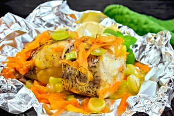 Pike with carrots, leeks, basil and lemon slices in a foil, a towel on the background of wooden boards