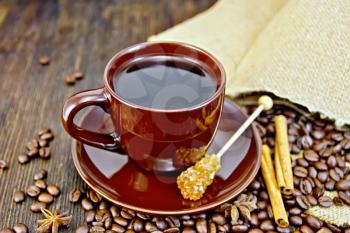Coffee in cup brown crystal sugar, a bag of coffee beans, cinnamon sticks and star anise on a wooden boards background