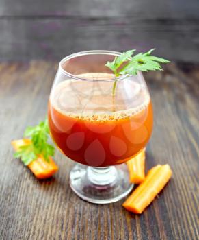 Carrot juice in a wineglass, slices of carrots and parsley on a wooden board background