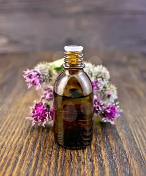 A glass bottle with oil, flowers and leaves of burdock against the background of wooden boards