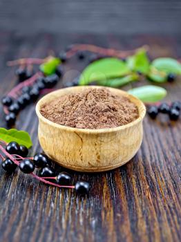 Flour of bird-cherry in a bowl with berries and leaves on a background of dark wooden boards