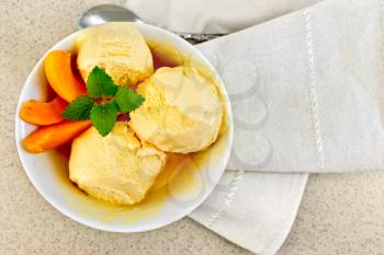 Apricot ice cream in a white bowl with slices of fruit, mint on a napkin on a background granite table top