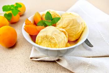 Apricot ice cream in a white bowl with slices of fruit, mint on a napkin on a background granite table
