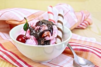 Ice cream cherry in a bowl, chocolate syrup and wafer rolls on a wooden boards background