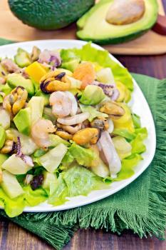 Salad with shrimp, octopus, mussels and calamari with avocado, lettuce and pineapple in a plate on a napkin on a dark wooden board