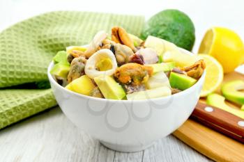 Salad with shrimp, octopus, mussels and calamari with avocado, lettuce, lemon and pineapple in a white bowl on the background light wooden boards