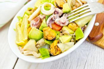 Salad with shrimp, octopus, mussels and calamari with avocado, lettuce, lemon and pineapple in a bowl on the background light wooden boards