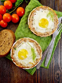 Two forms of tartlets with meat and eggs in the forms on a napkin, tomatoes, bread, parsley and dill on background of wood planks top