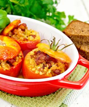 Tomatoes stuffed with meat and steamed wheat bulgur in a roasting pan on a napkin, bread and parsley on a wooden board background