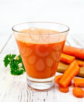 Carrot juice in a tall glass, vegetables with parsley on a wooden boards background