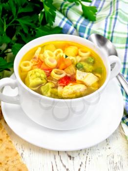 Minestrone soup with meat, celery, tomatoes, zucchini and cabbage, green peas, carrots and pasta in a bowl, towel, bread on the background light wooden boards