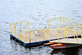 Pierce with yellow railings and wooden flooring with spinning, white plastic chair on the water