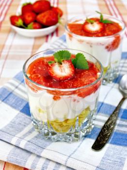 Dairy dessert with strawberries, corn flakes and yogurt in two glassful, spoon, blue napkin, berries in a bowl on linen tablecloth background