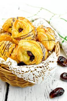 Cookies with dates in a wicker basket with a napkin, fruit and towel on light background wooden plank