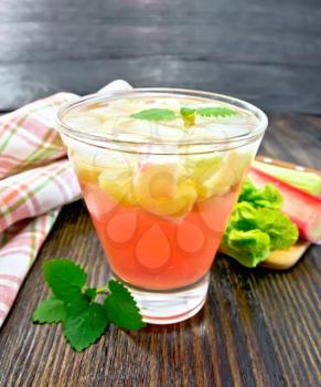 Lemonade with rhubarb and mint in a glass, stems and a leaf of a vegetable, napkin on a wooden plank background