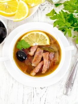 Soup saltwort with lemon, meat, pickles, tomato sauce and olives in a white bowl on a wooden board background top