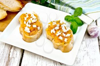 Bruschetta with pumpkin, salted feta cheese in a plate, garlic, basil and parsley, napkin and orange vegetable on a wooden board background