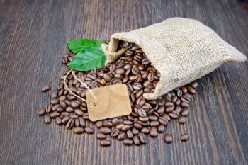 Bag of black coffee beans, tag and green leaves on a wooden board background