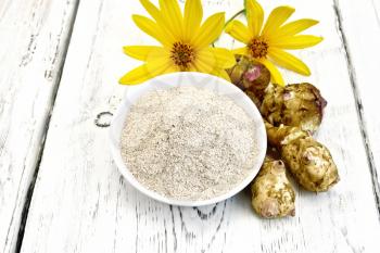 Flour of Jerusalem artichoke in a bowl with flowers and vegetables on the background of wooden boards