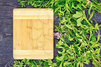 Frame of leaves herbs of fenugreek, rue, savory, tarragon, thyme and rectangular board on the background of a wooden table
