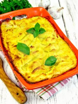 Casserole from mashed potatoes with fish fillets in a brazier on a towel on a wooden plank background