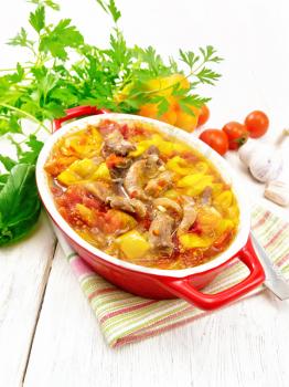 Ragout of turkey meat, tomato, yellow sweet pepper and onion with sauce in a brazier on a towel on the background of a wooden board