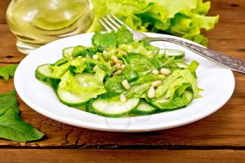 Salad from spinach, fresh cucumbers, rukkola salad, cedar nuts and spring onions, seasoned with vegetable oil and a fork on a plate on the background of the board
