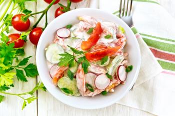 Salad of fresh tomatoes, cucumbers and radish with green onions and parsley,  flavored with mayonnaise and sour cream in a plate, towel and fork on a wooden board background on top