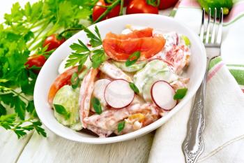 Salad of fresh tomatoes, cucumbers and radish with green onions and parsley,  flavored with mayonnaise and sour cream in a plate, napkin and fork on a wooden plank background