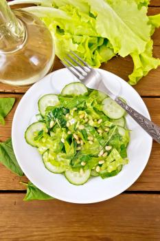 Salad from spinach, fresh cucumbers, rukkola salad, cedar nuts and spring onions, seasoned with vegetable oil and spices with a fork on a plate on a wooden board background