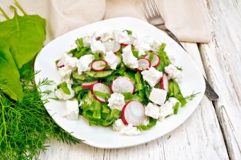 Salad with spinach, cucumbers, radish and salted cheese, dill and green onions in a plate, a towel on the background of a wooden board