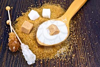 Sugar white and brown in cubes, granulated in a spoon and crystal on a stick against a dark wooden board