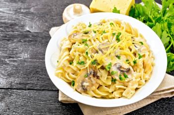 Fusilli pasta with mushrooms in creamy sauce, parsley and grated cheese in a plate on napkin on black wooden board background